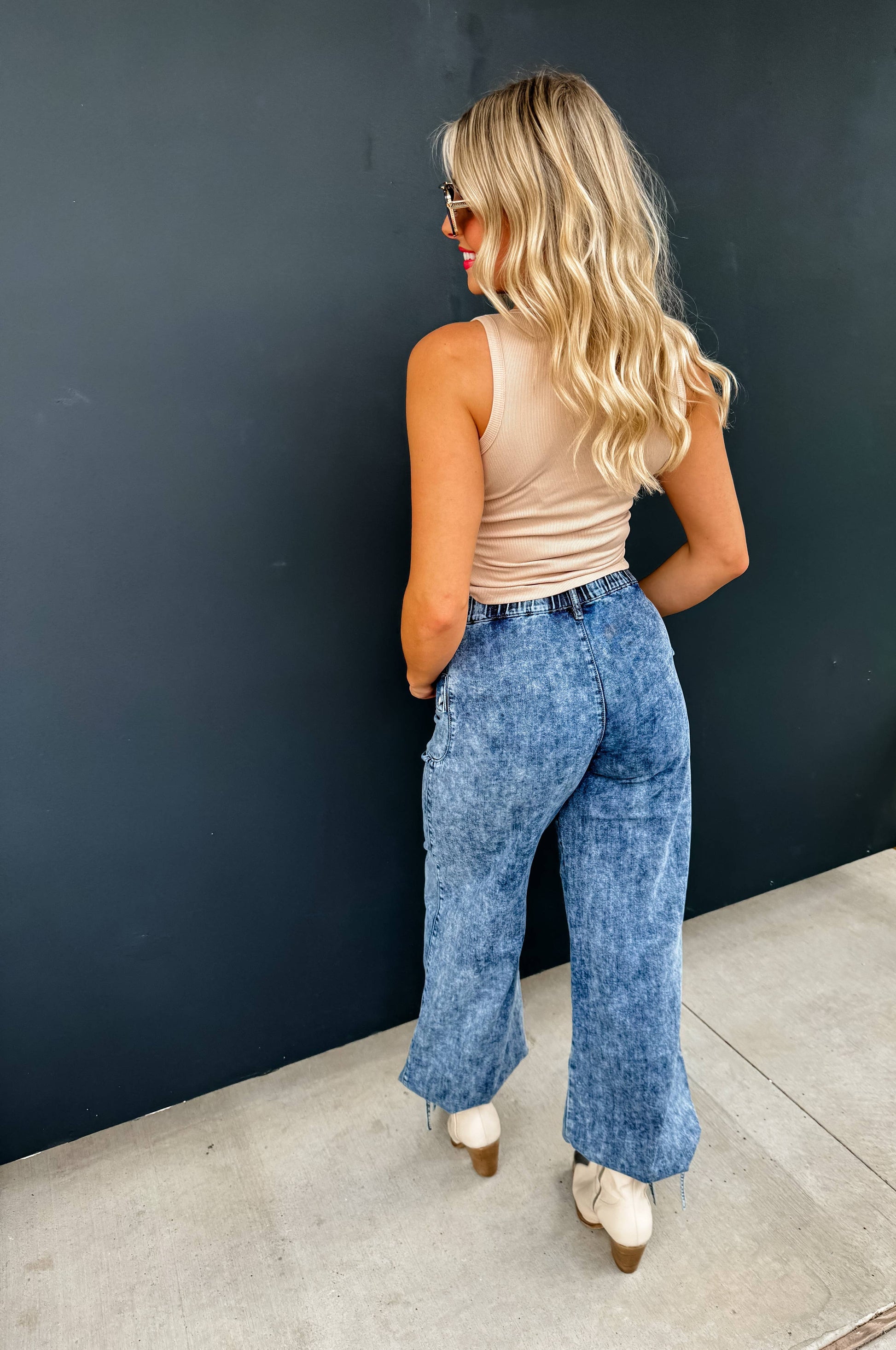 Back view of a model wearing Charlie Cinch Hem Wide Leg Jeans in light blue denim with a beige tank.