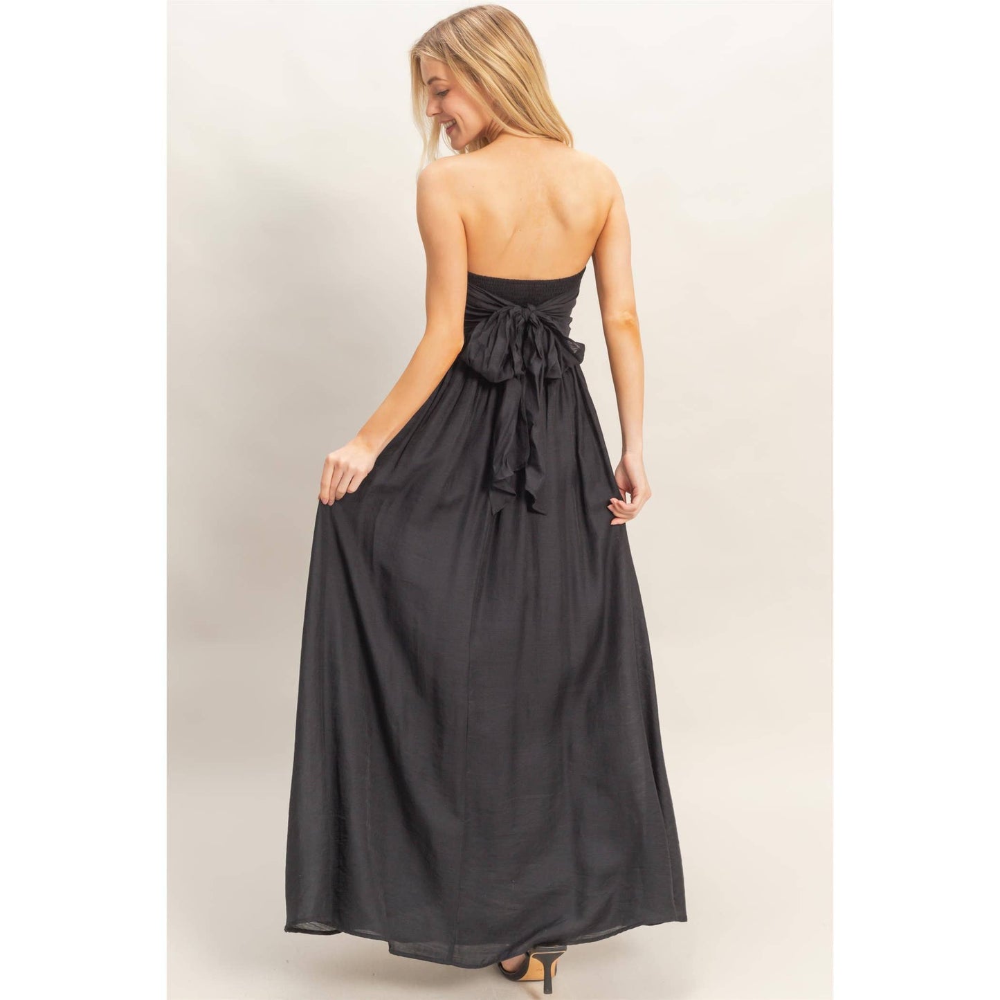 Back view of a strapless tie-back smocked dress in black with a large bow at the back.