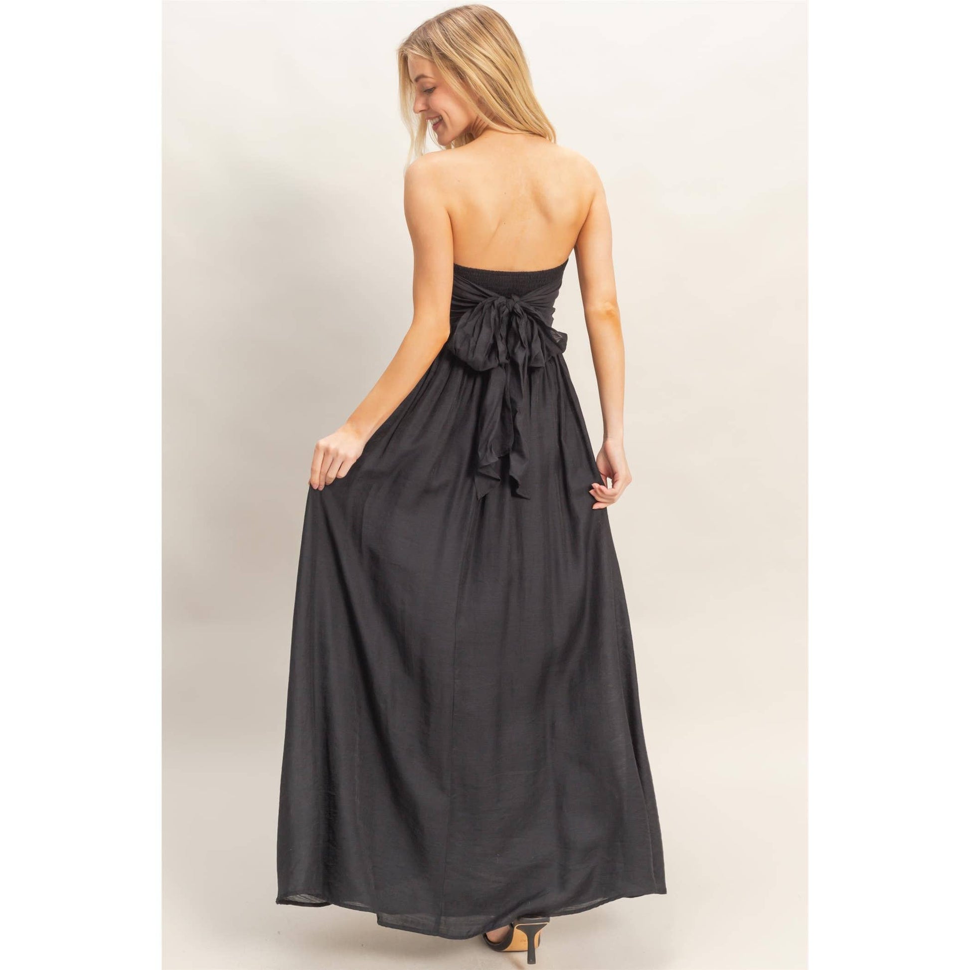 Back view of a strapless tie-back smocked dress in black with a large bow at the back.