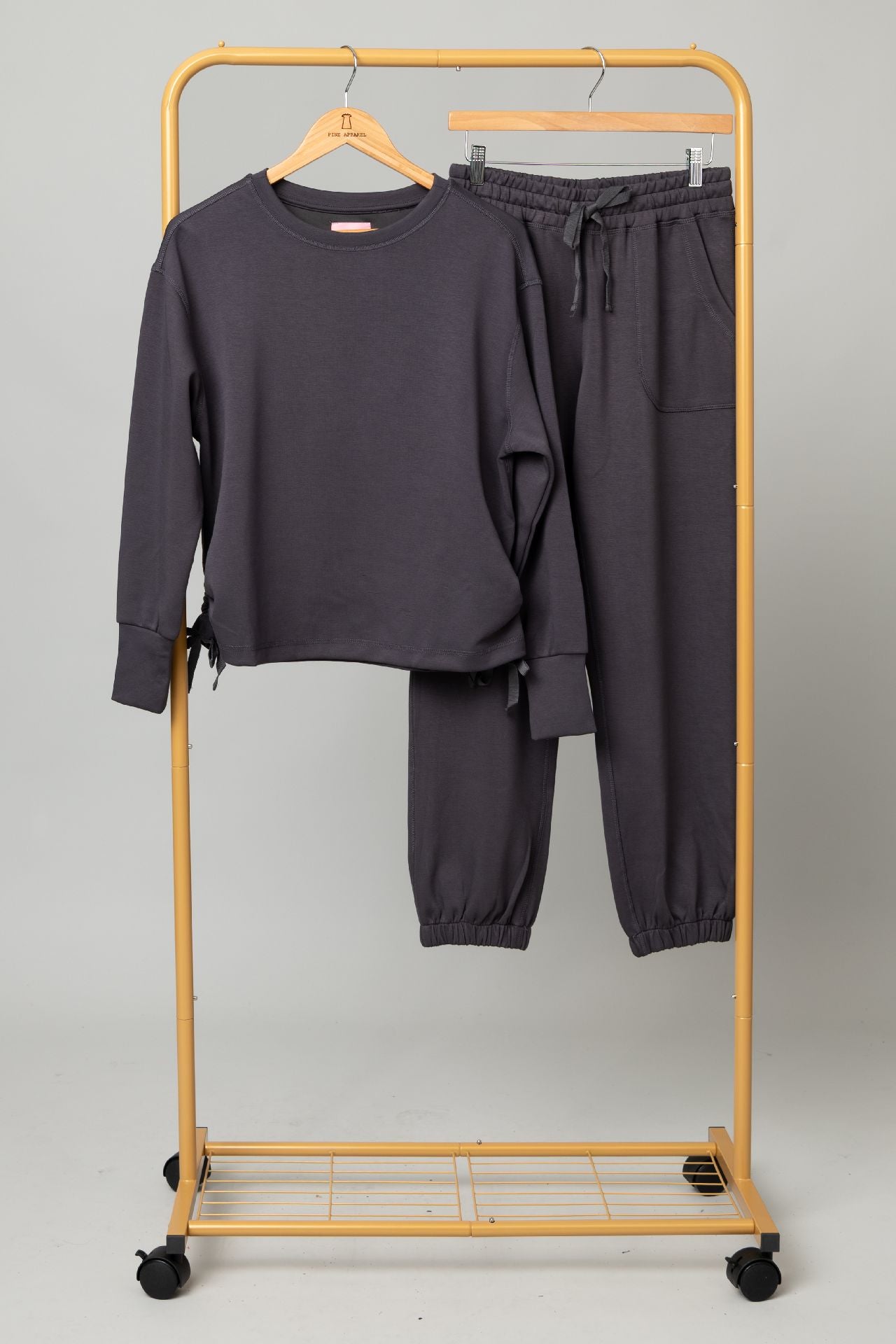 Sport Lux Set: dark charcoal long-sleeve top with matching jogger pants on a gold clothing rack.