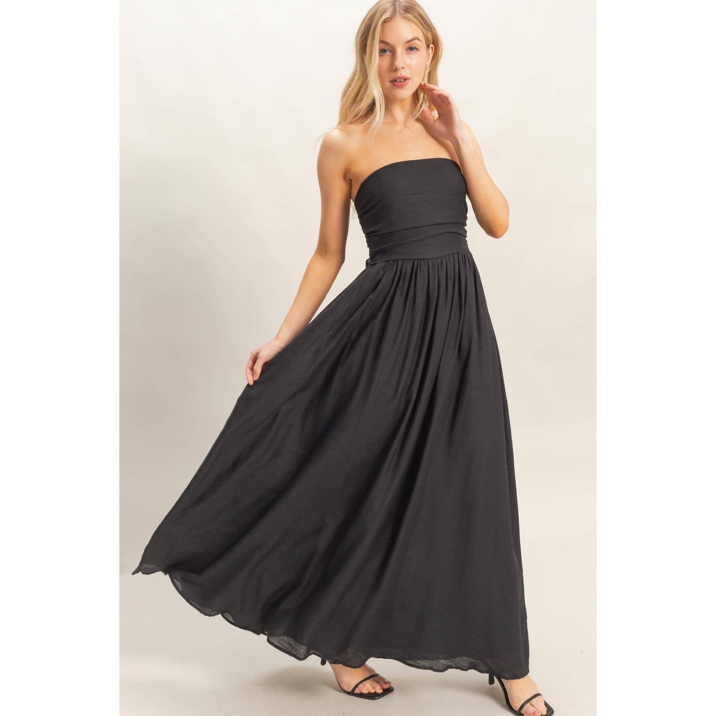 Model in strapless black smocked dress with a back tie and flowing skirt.