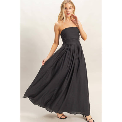 Model in strapless black smocked dress with a back tie and flowing skirt.
