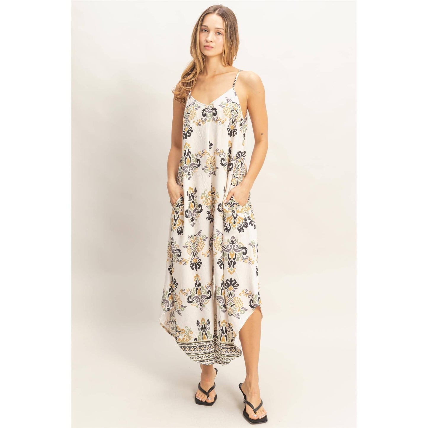 Model wearing a floral print spaghetti-strap jumpsuit with a flowing silhouette and black sandals.