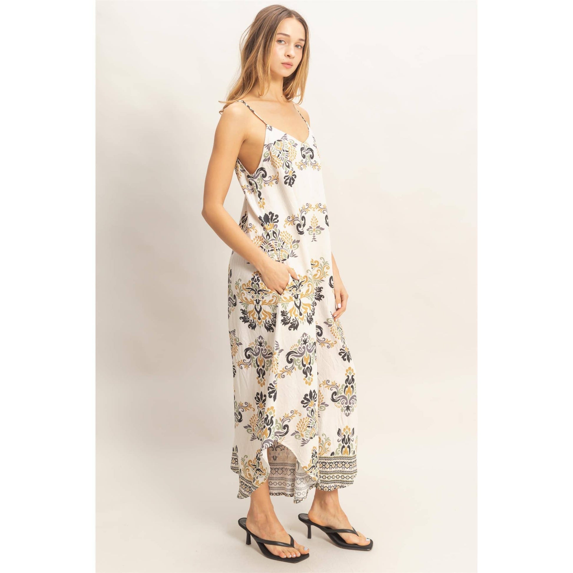 Model in flowy floral print spaghetti jumpsuit with adjustable straps, paired with black sandals.