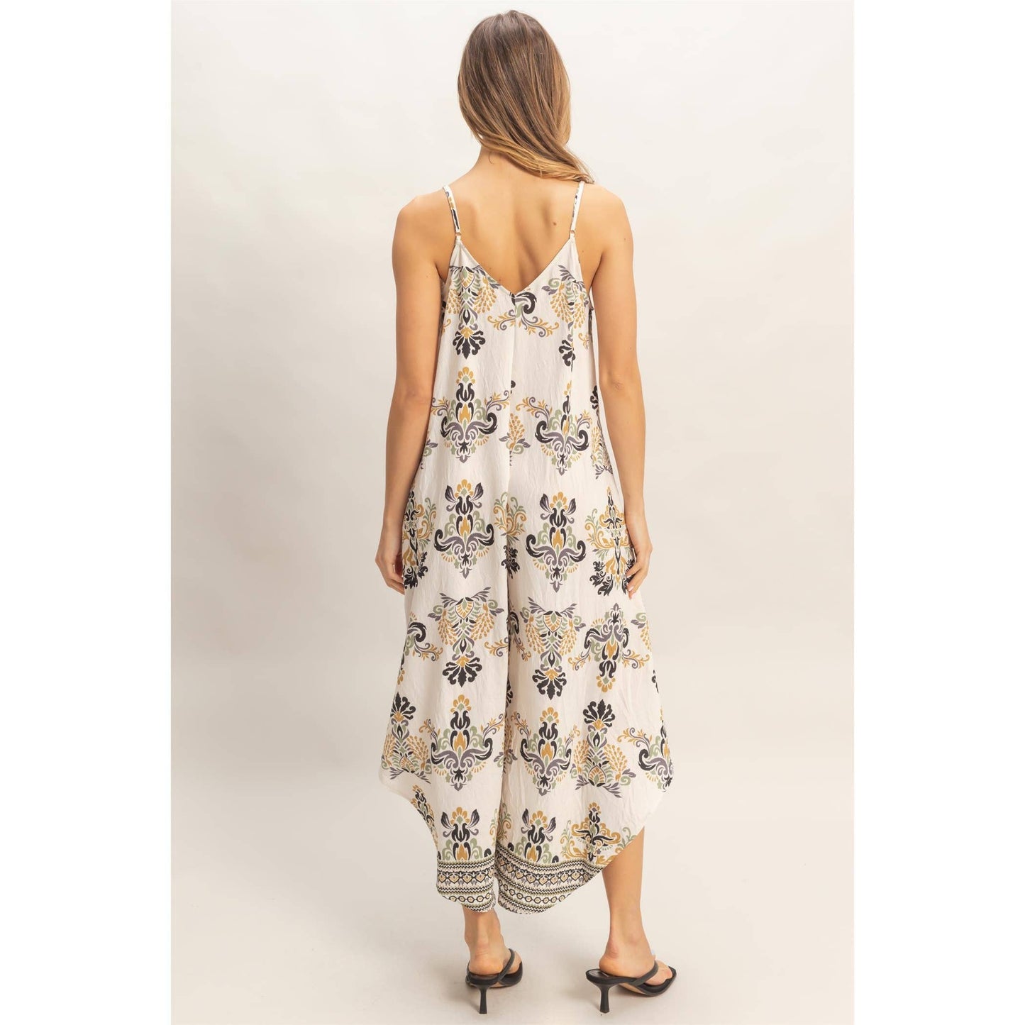 Back view of a model wearing a flowy floral print spaghetti-strap jumpsuit.
